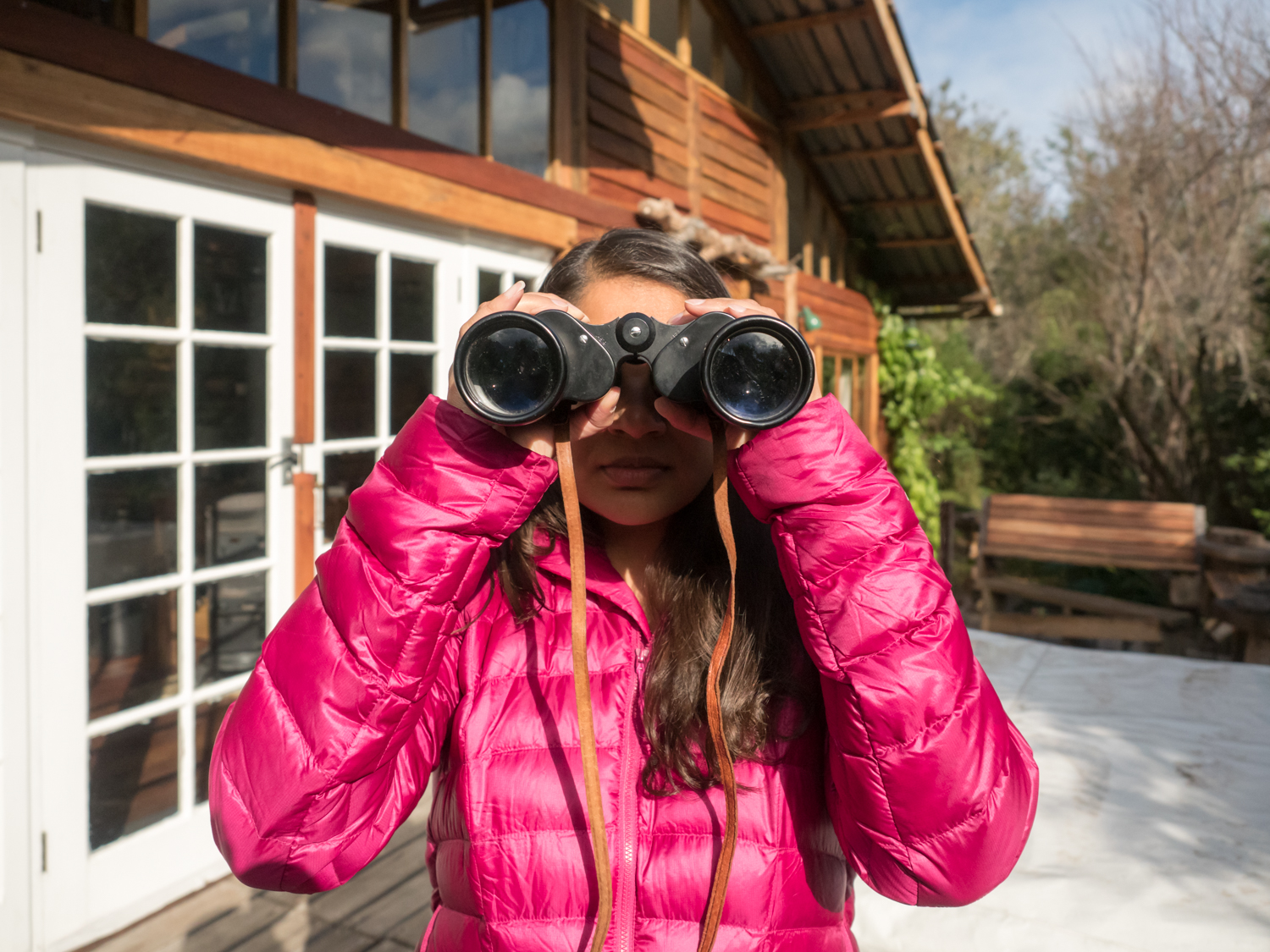 The photographer in a magenta jacket looks through a pair of large, old binoculars